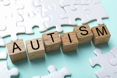 Photo of Word Autism made with wooden cubes and puzzle pieces on light blue background, closeup