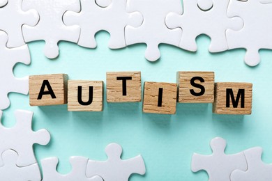 Photo of Word Autism made with wooden cubes and puzzle pieces on light blue background, flat lay