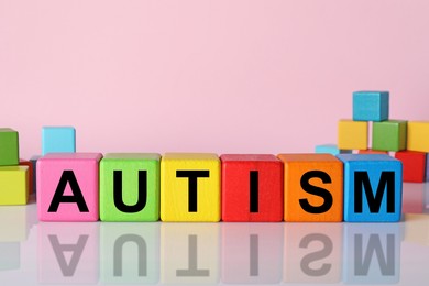 Photo of Word Autism made of colorful cubes against pink background