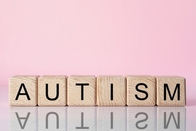 Photo of Word Autism made of wooden cubes against pink background, space for text