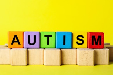 Photo of Word Autism made of colorful cubes on yellow background, space for text