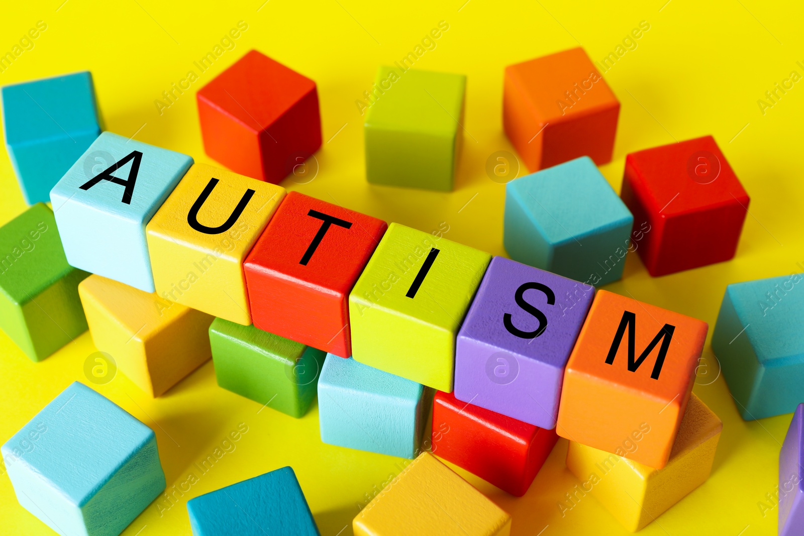 Photo of Word Autism made of colorful cubes on yellow background, closeup