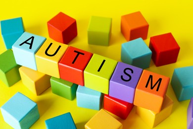 Photo of Word Autism made of colorful cubes on yellow background, closeup