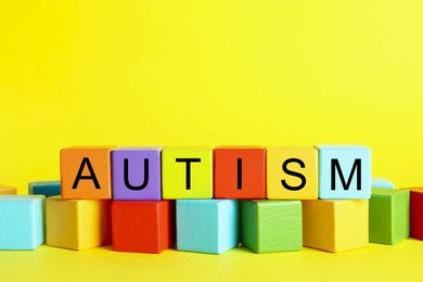 Photo of Word Autism made of colorful cubes on yellow background, space for text