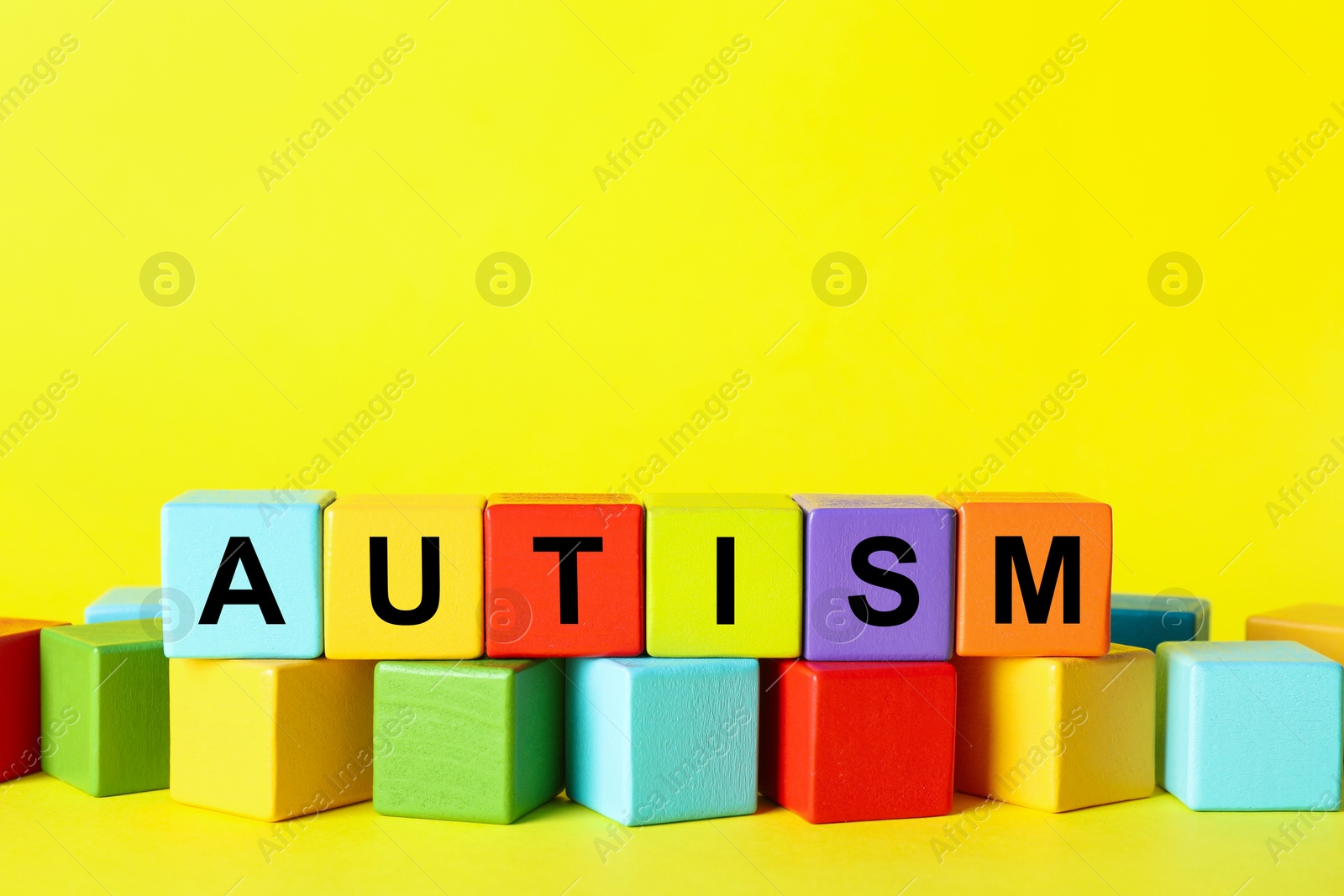 Photo of Word Autism made of colorful cubes on yellow background, space for text