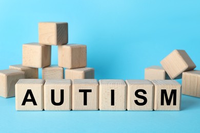 Photo of Word Autism made of wooden cubes on light blue background