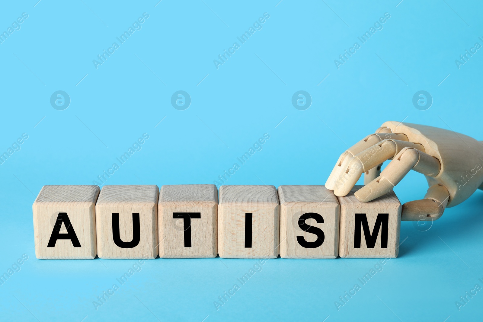 Photo of Word Autism made of wooden cubes and mannequin hand on light blue background, space for text