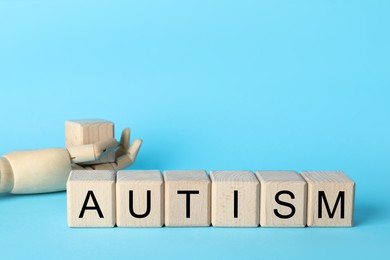 Photo of Word Autism made of wooden cubes and mannequin hand on light blue background, space for text