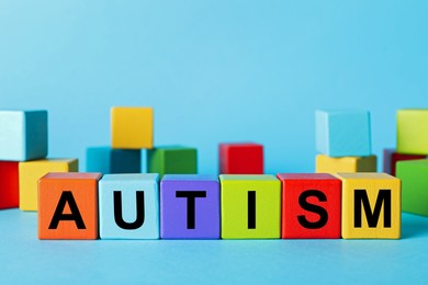 Photo of Word Autism made of colorful cubes on light blue background