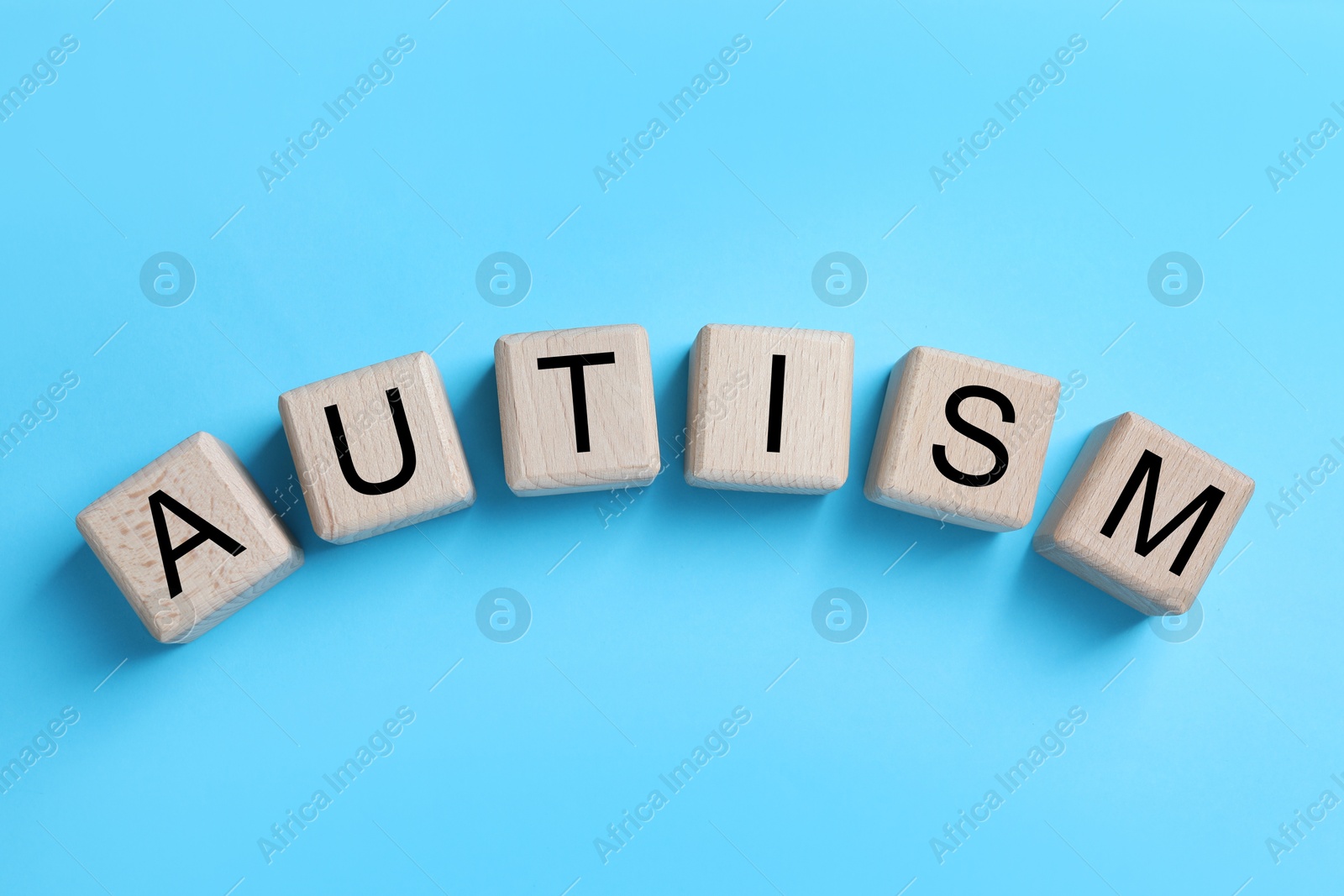 Photo of Word Autism made of wooden cubes on light blue background, top view