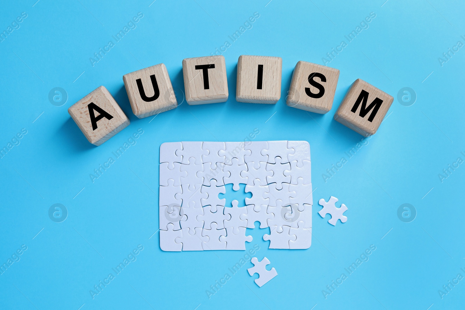 Photo of Word Autism made of wooden cubes and puzzle on light blue background, top view