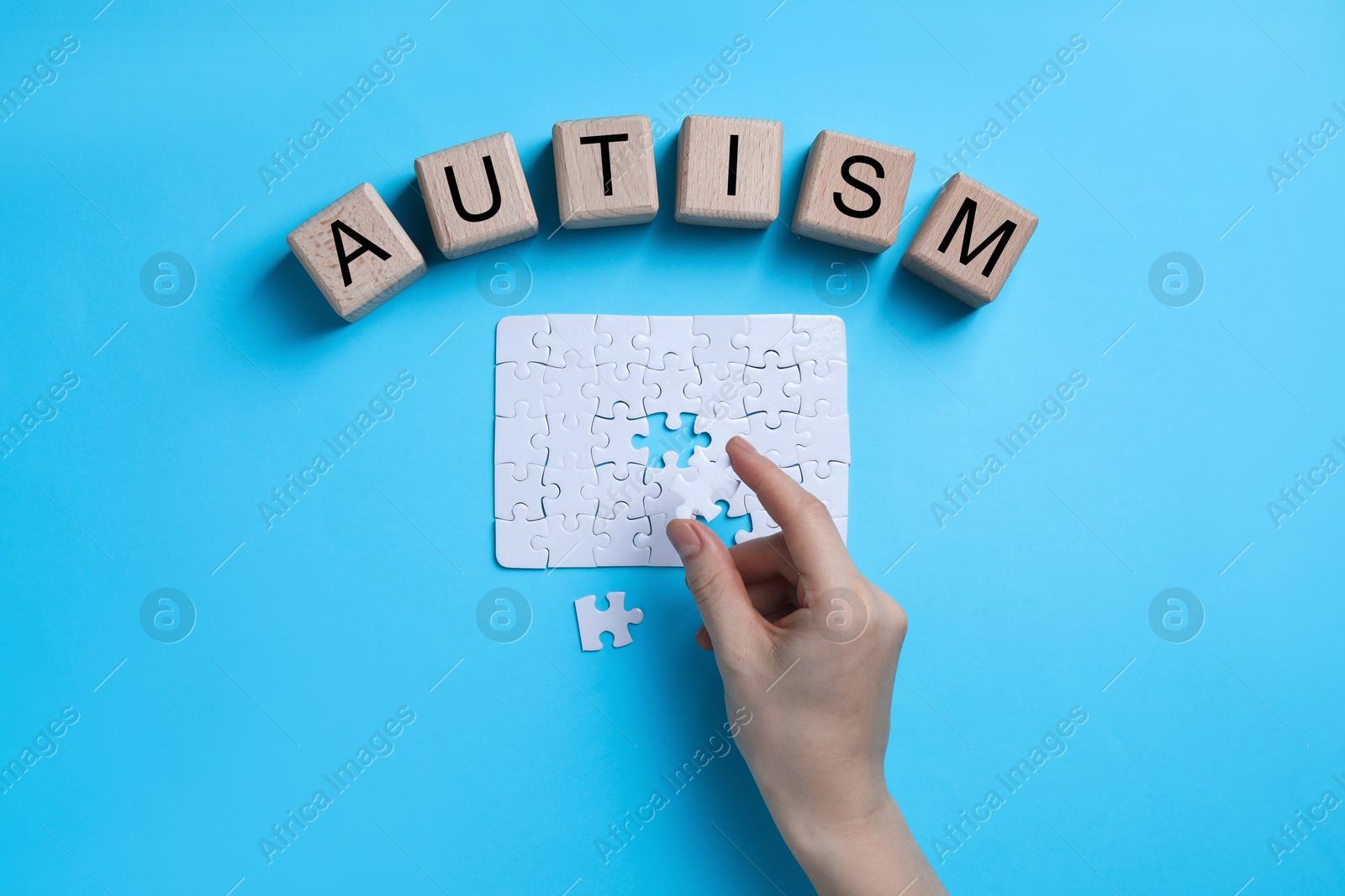 Photo of Word Autism made of wooden cubes. Woman solving puzzle on light blue background, top view