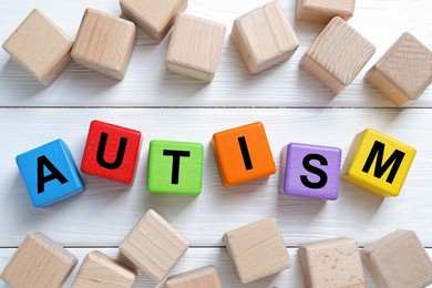 Photo of Word Autism made of colorful cubes on white wooden background, top view