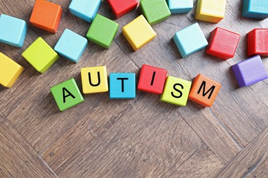 Photo of Word Autism made of colorful cubes on wooden background, top view. Space for text