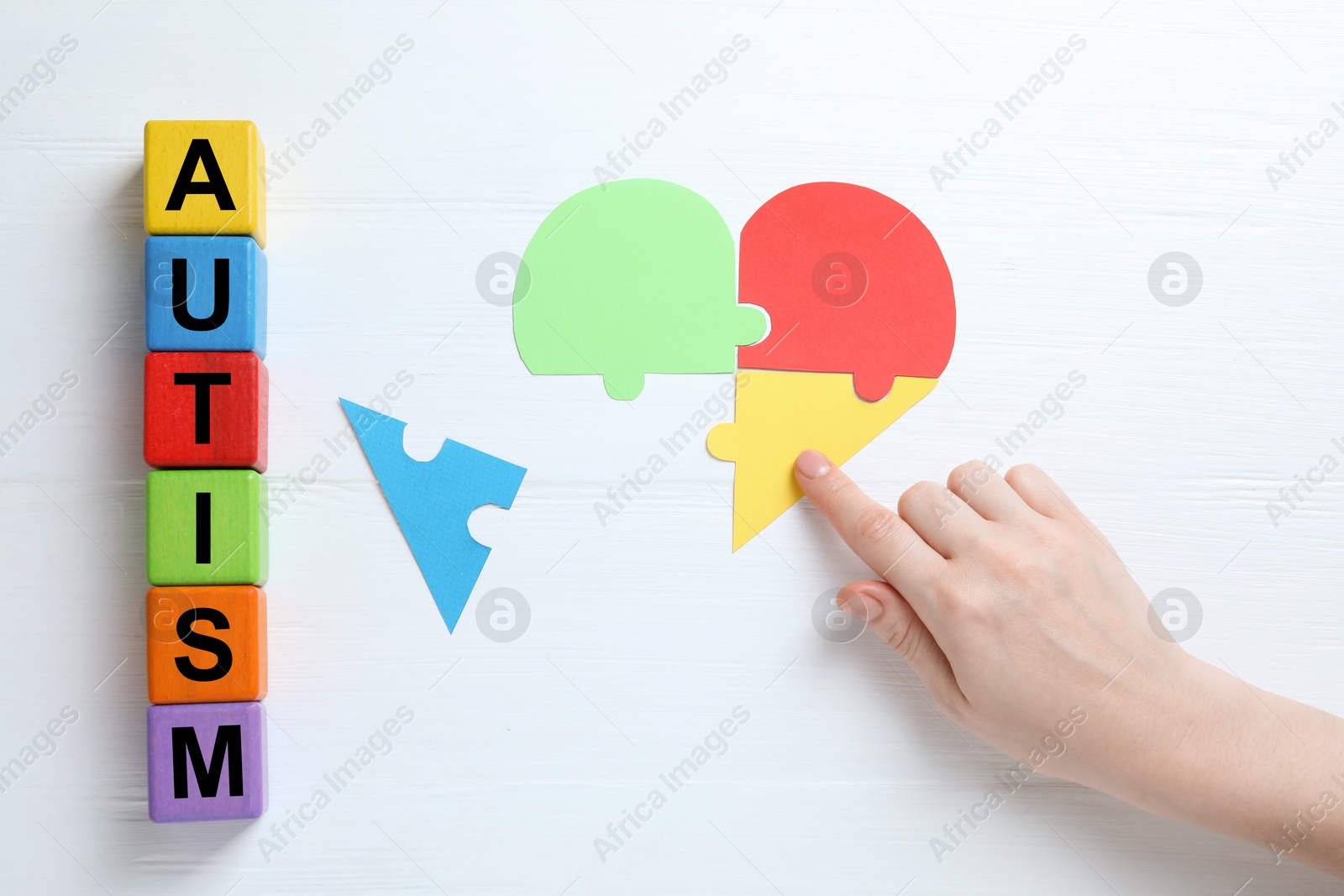 Photo of Word Autism made of colorful cubes. Woman playing with puzzle on white wooden background, top view