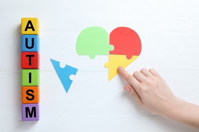 Photo of Word Autism made of colorful cubes. Woman playing with puzzle on white wooden background, top view