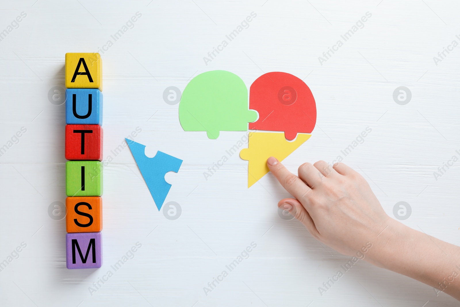 Photo of Word Autism made of colorful cubes. Woman playing with puzzle on white wooden background, top view