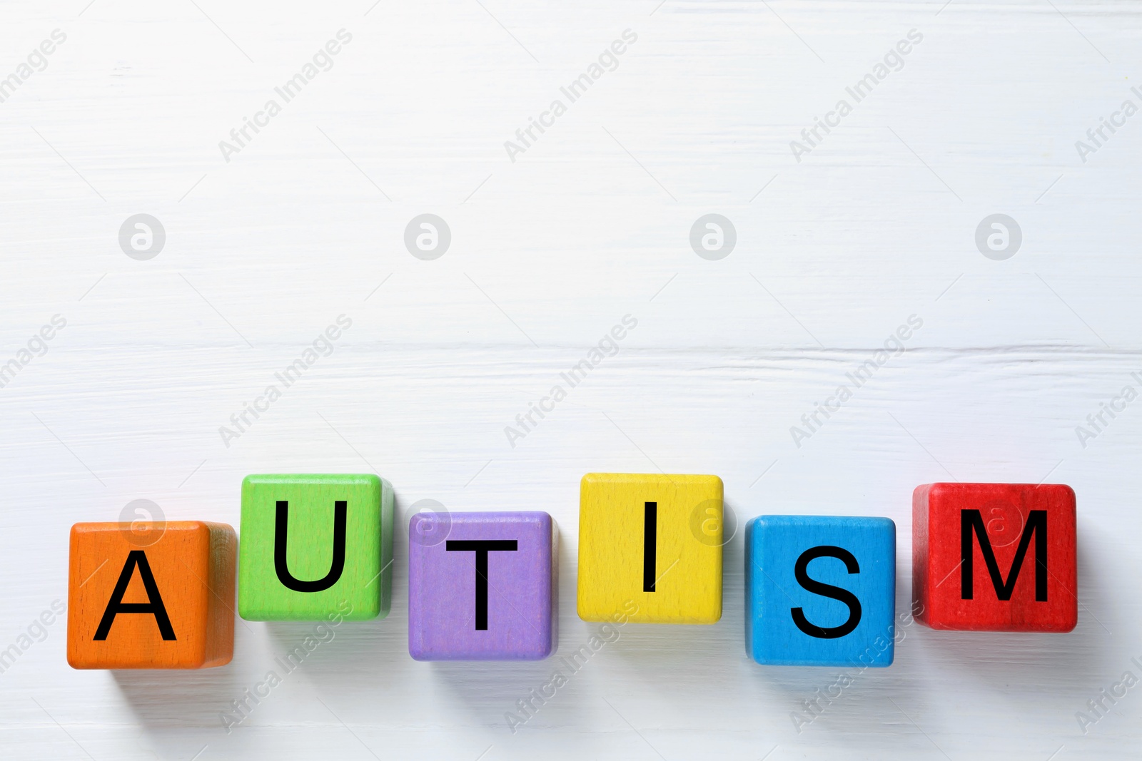 Photo of Word Autism made of colorful cubes on white wooden background, top view. Space for text