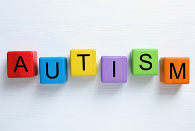 Photo of Word Autism made of colorful cubes on white wooden background, top view