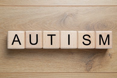 Photo of Word Autism made of cubes on wooden background, top view