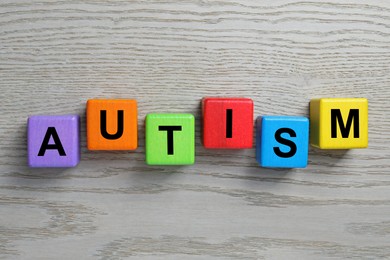 Photo of Word Autism made of colorful cubes on wooden background, top view