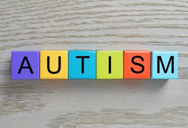 Photo of Word Autism made of colorful cubes on wooden background, top view