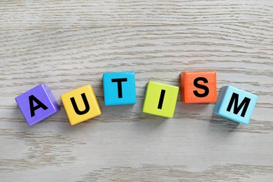 Photo of Word Autism made of colorful cubes on wooden background, top view