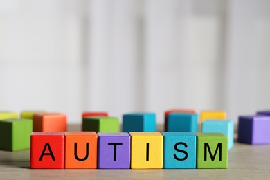 Photo of Word Autism made of colorful cubes on wooden table against blurred background, space for text