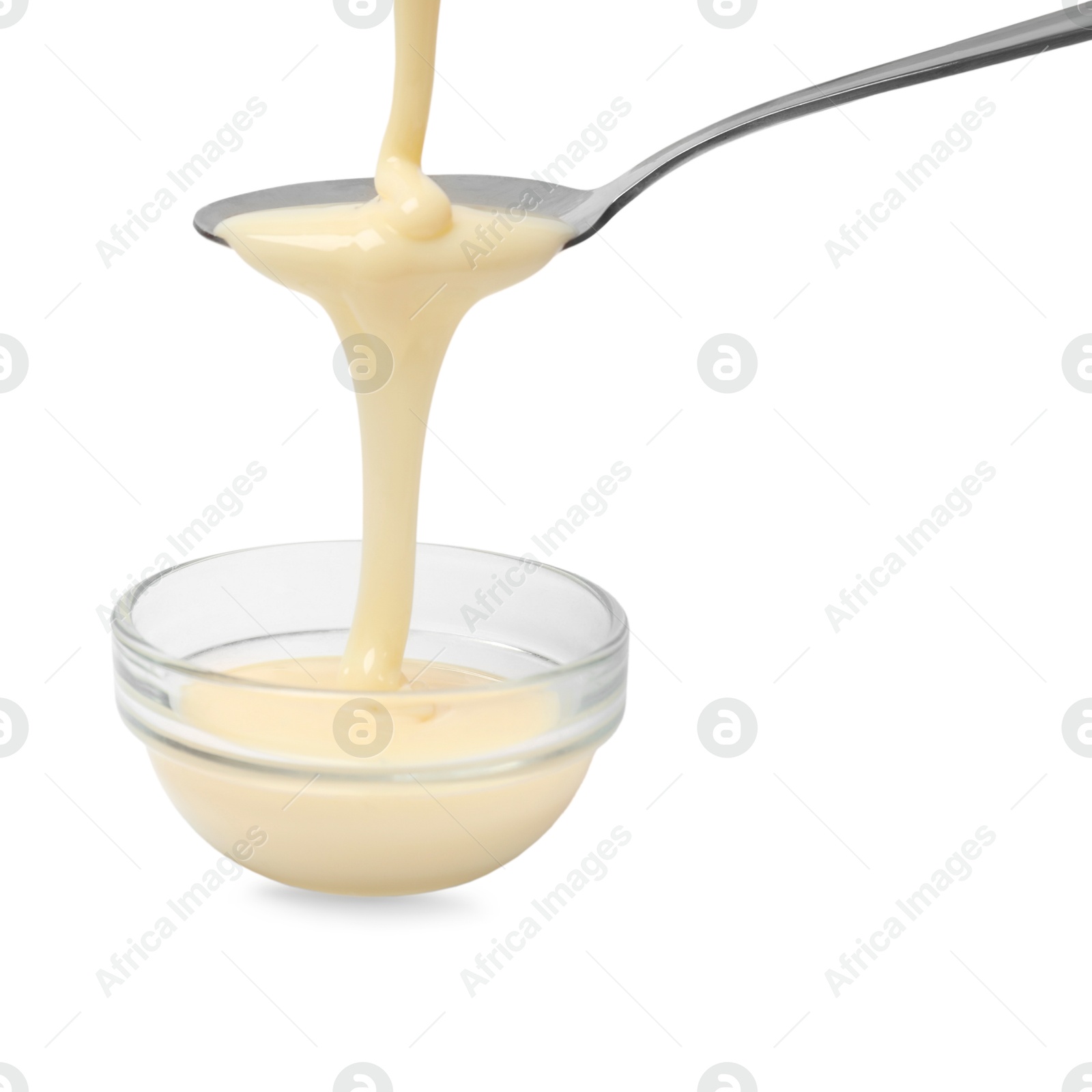 Photo of Condensed milk flowing down from spoon into bowl isolated on white