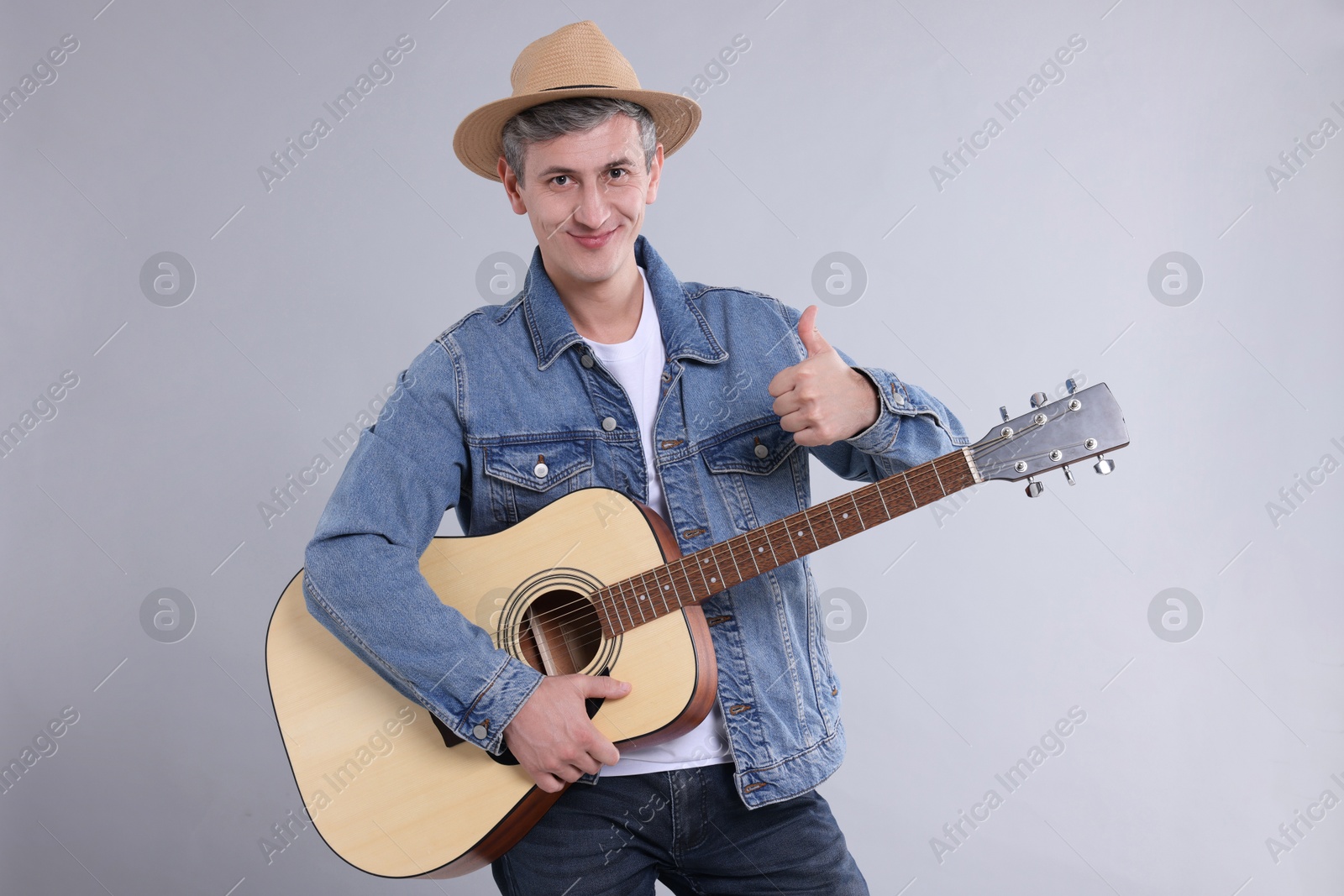 Photo of Happy man with guitar showing thumbs up on light grey background