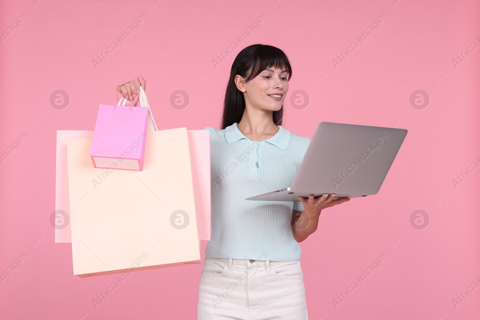 Photo of Internet shopping. Happy woman with laptop and colorful bags on pink background