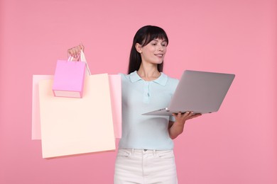 Photo of Internet shopping. Happy woman with laptop and colorful bags on pink background