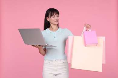 Photo of Internet shopping. Happy woman with laptop and colorful bags on pink background