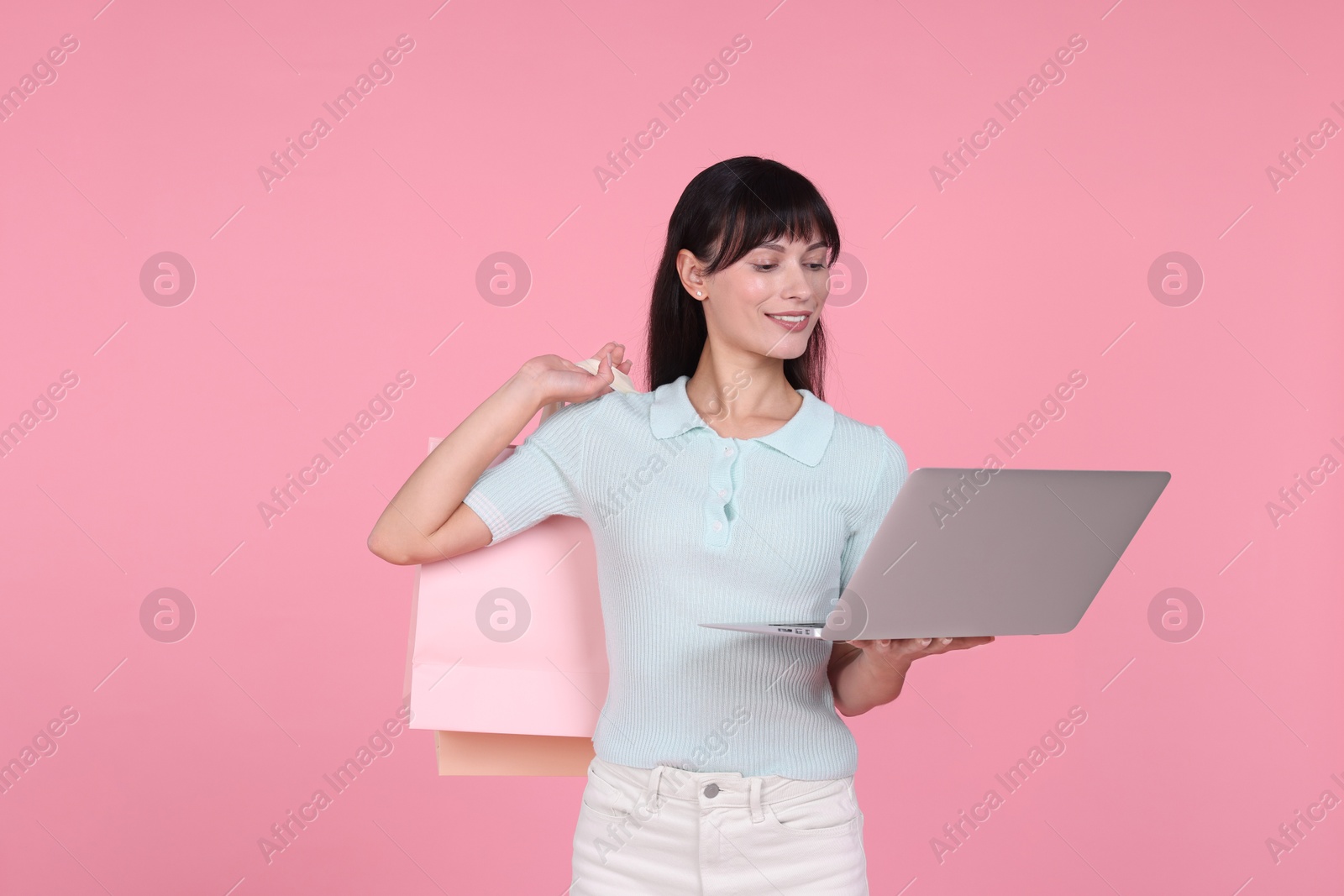 Photo of Internet shopping. Happy woman with laptop and colorful bags on pink background