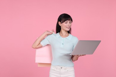 Photo of Internet shopping. Happy woman with laptop and colorful bags on pink background