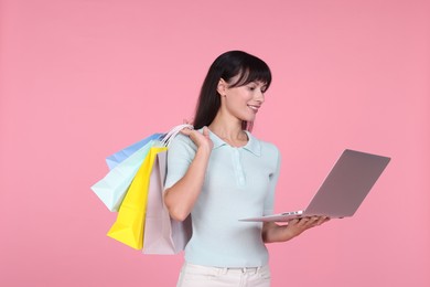 Photo of Internet shopping. Happy woman with laptop and colorful bags on pink background