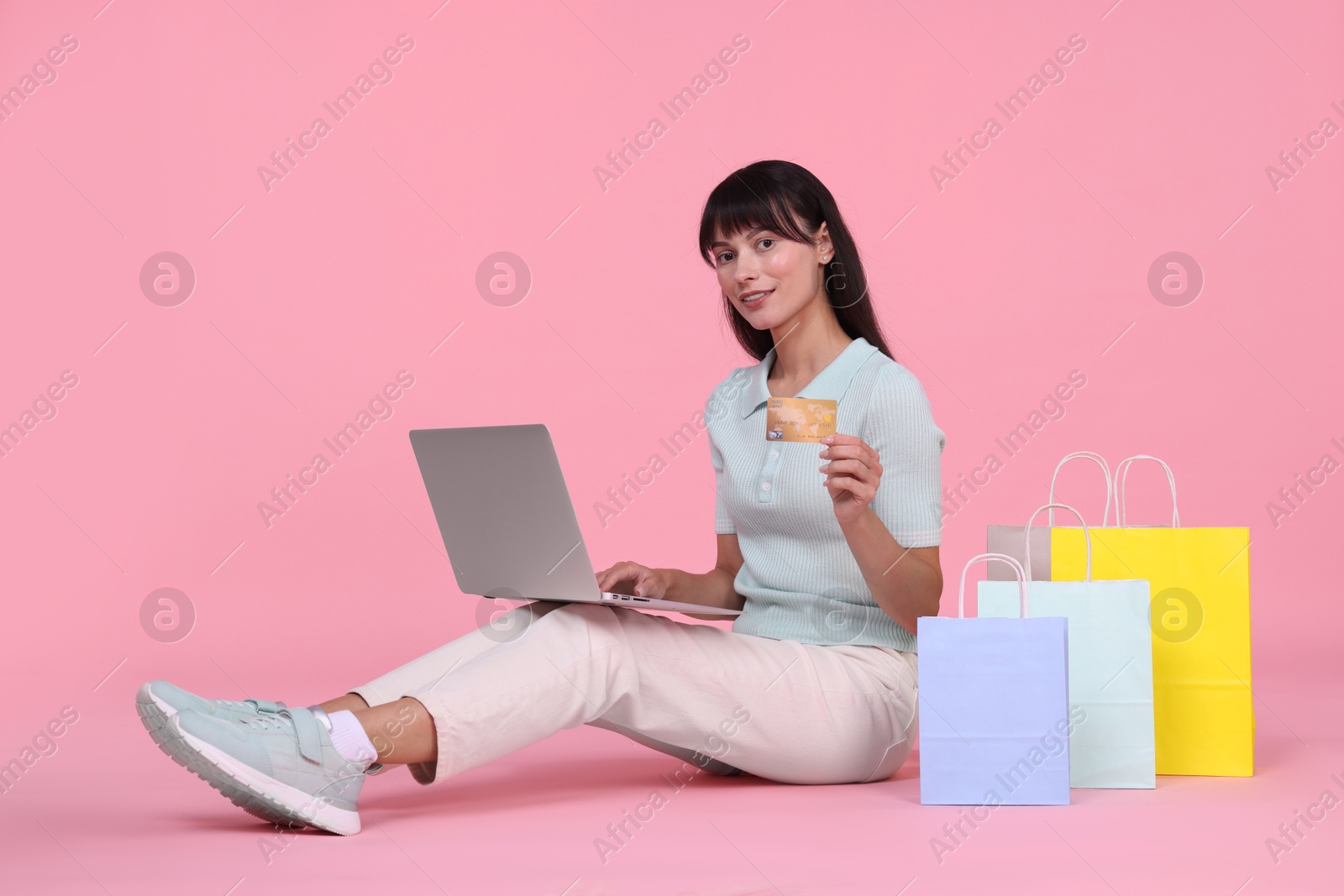 Photo of Internet shopping. Happy woman with credit card, laptop and colorful bags on pink background