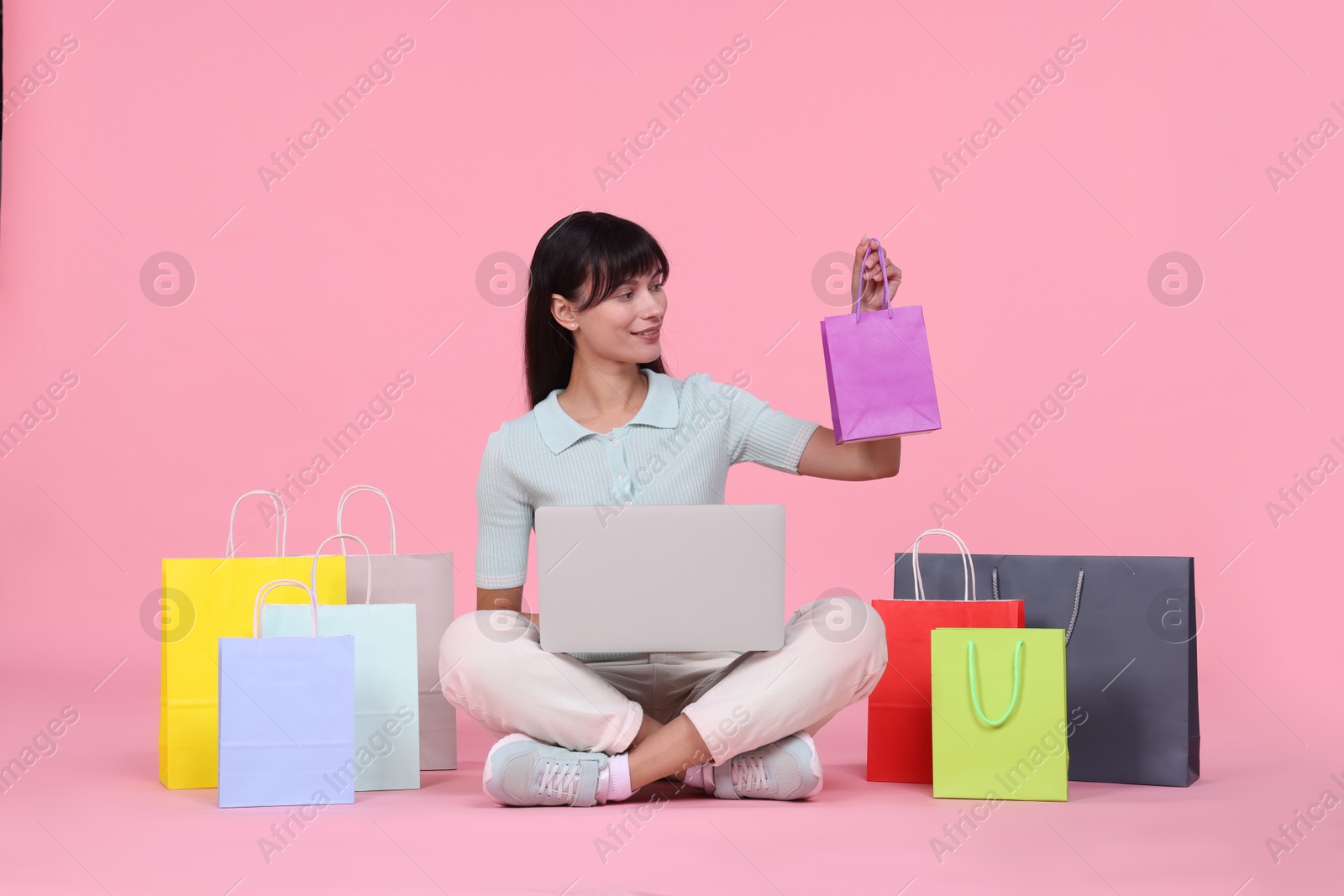 Photo of Internet shopping. Happy woman with laptop and colorful bags on pink background