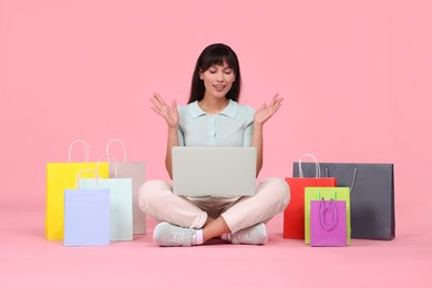 Photo of Internet shopping. Happy woman with laptop and colorful bags on pink background