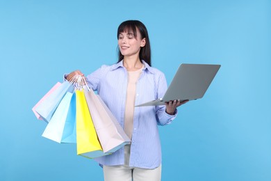 Photo of Internet shopping. Happy woman with laptop and colorful bags on light blue background