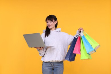 Photo of Internet shopping. Happy woman with laptop and colorful bags on orange background