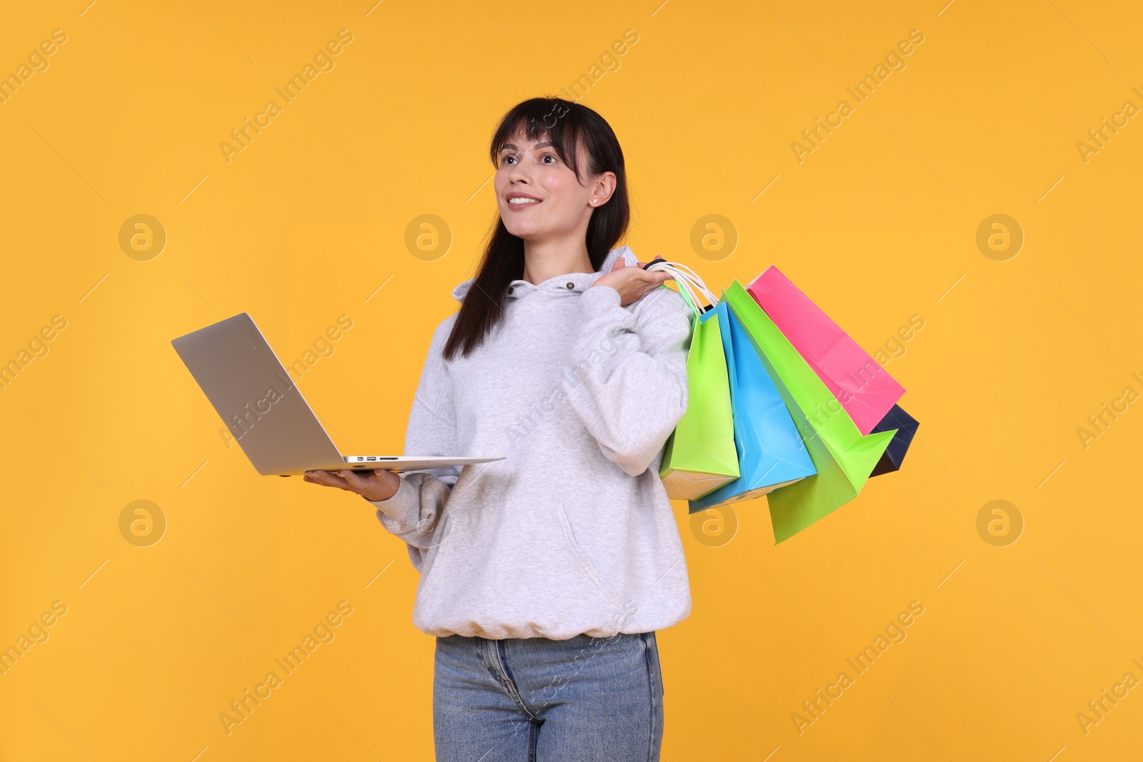 Photo of Internet shopping. Happy woman with laptop and colorful bags on orange background