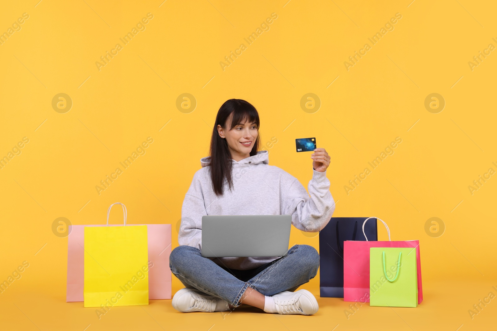 Photo of Internet shopping. Happy woman with credit card, laptop and colorful bags on orange background