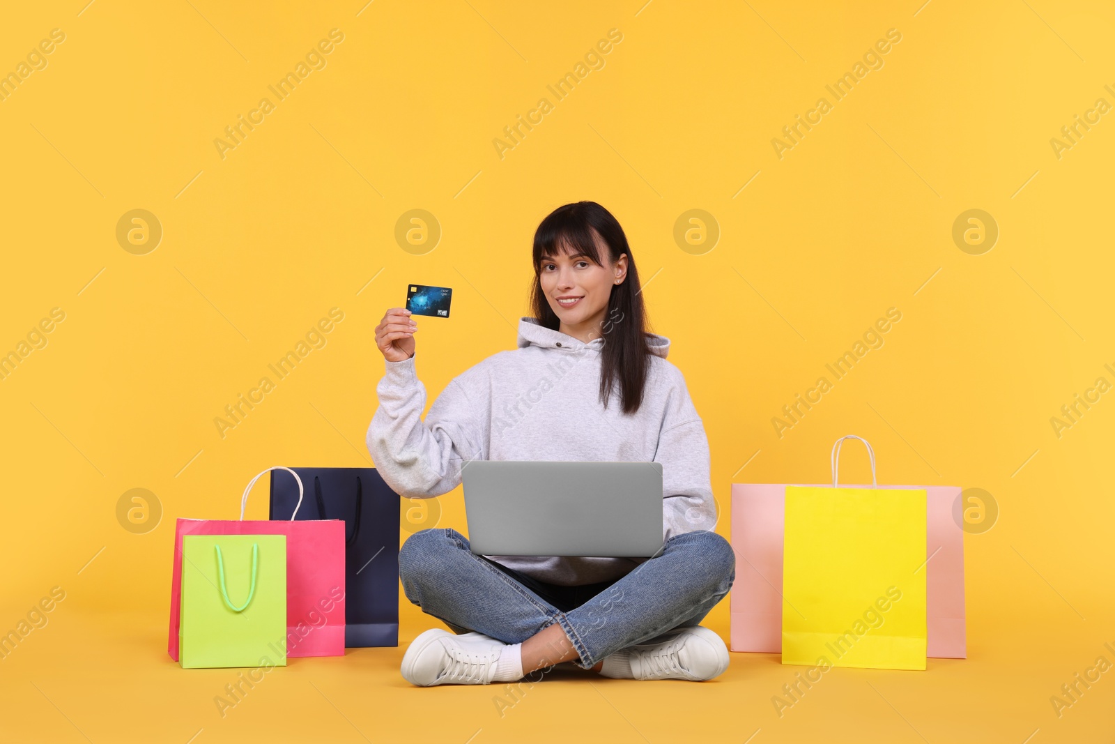 Photo of Internet shopping. Happy woman with credit card, laptop and colorful bags on orange background