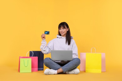 Photo of Internet shopping. Happy woman with credit card, laptop and colorful bags on orange background