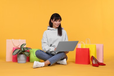 Photo of Internet shopping. Happy woman with laptop and colorful bags on orange background