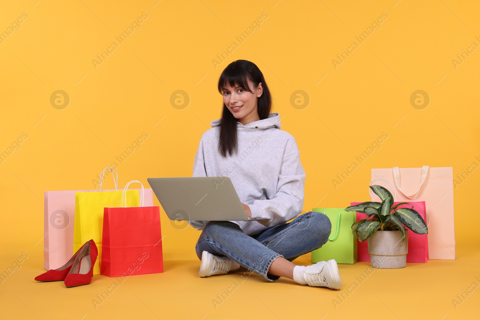 Photo of Internet shopping. Happy woman with laptop and colorful bags on orange background