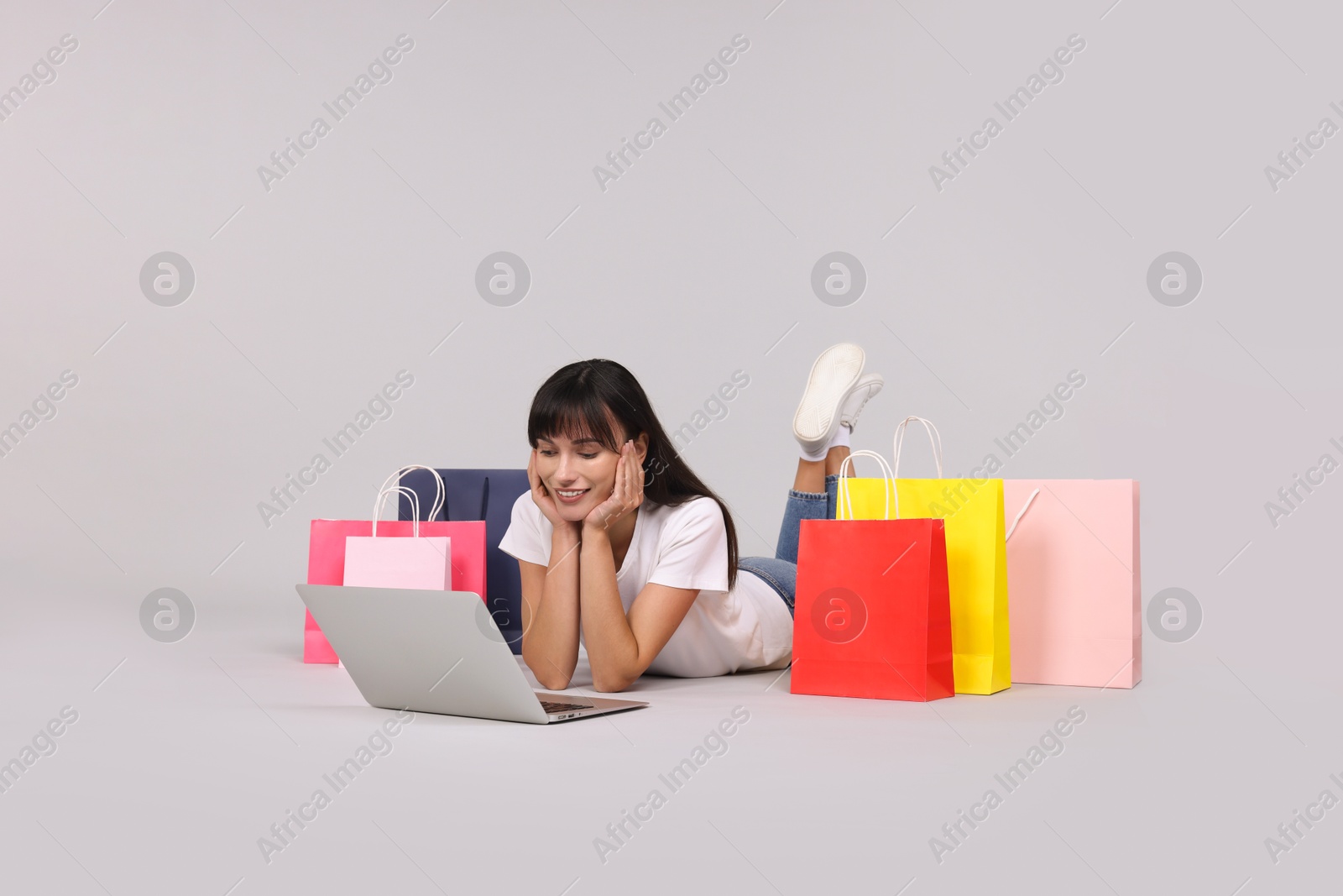 Photo of Internet shopping. Happy woman with laptop and colorful bags on grey background