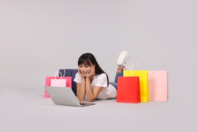 Photo of Internet shopping. Happy woman with laptop and colorful bags on grey background