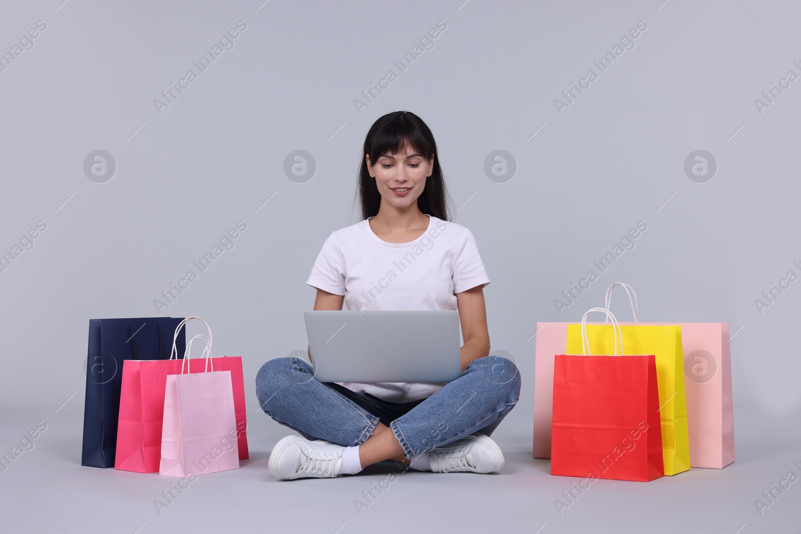 Photo of Internet shopping. Happy woman with laptop and colorful bags on grey background